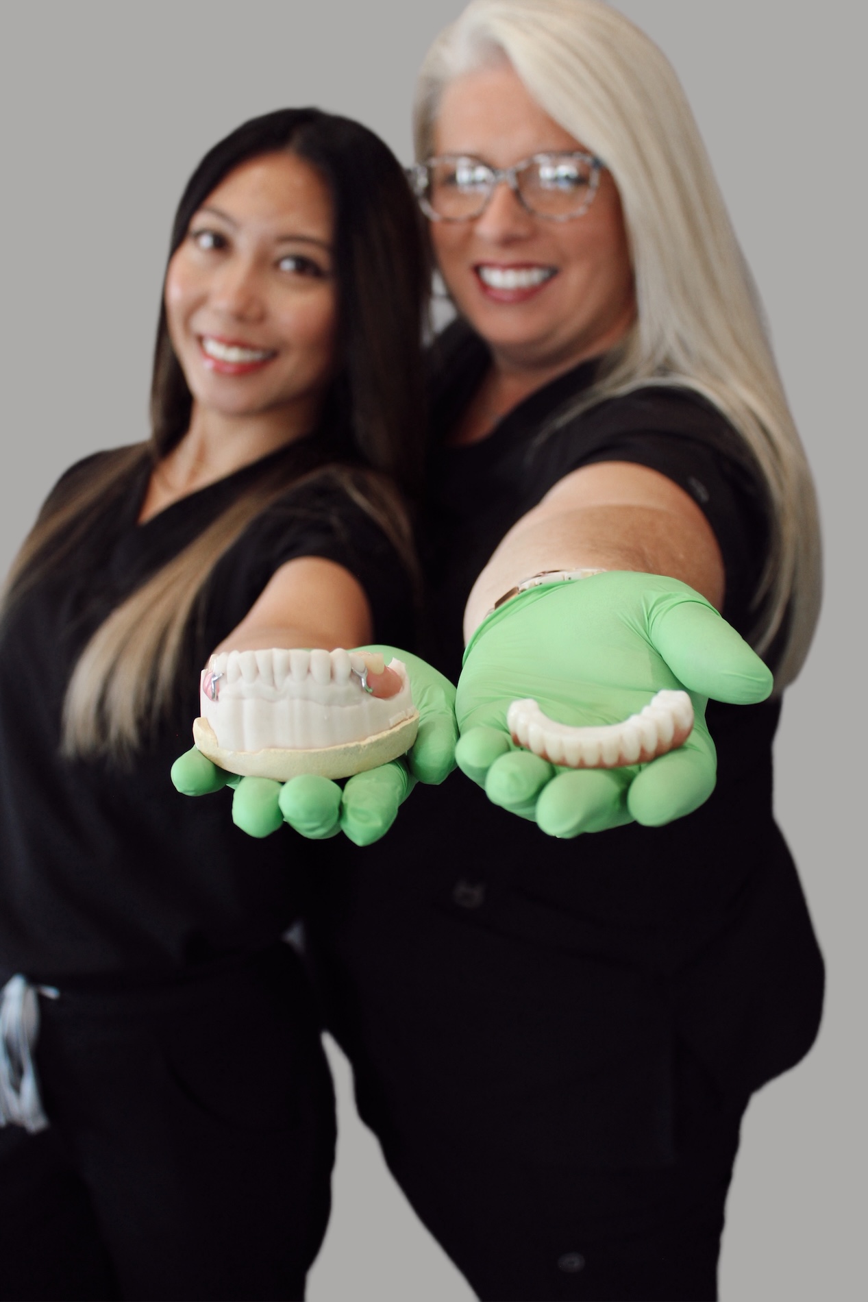 Two dental professionals holding up their hands with dental models in their gloves, standing against a white background.