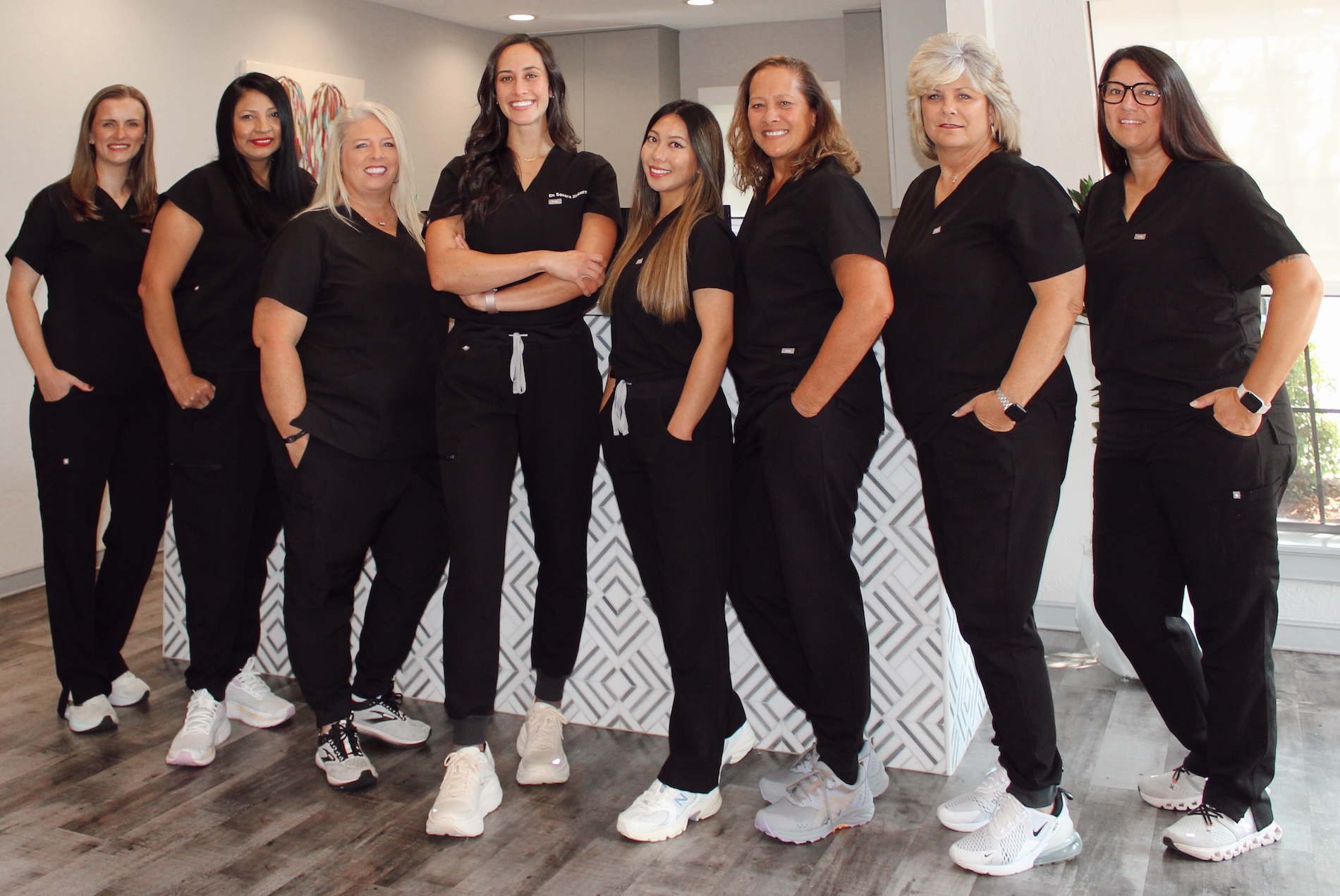 A group of professional women wearing scrubs, posing together with smiles for a photo.