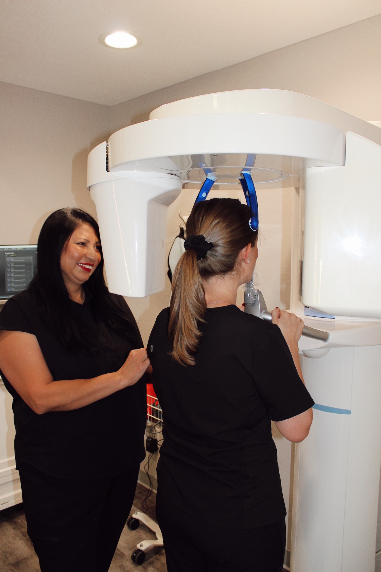 A woman stands next to a large, white, medical CT scanner, while another person appears to be examining the equipment.