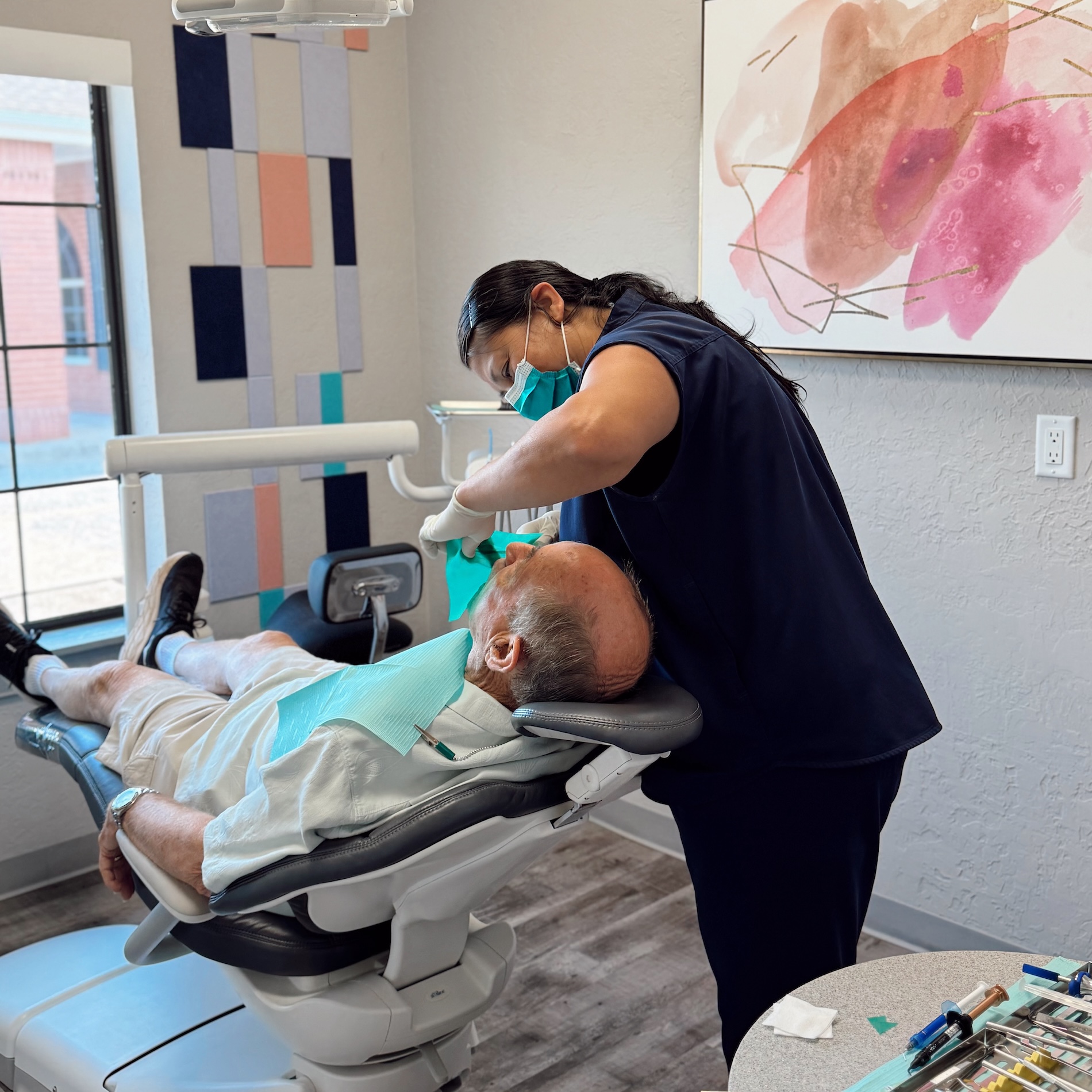 A dental office setting with a dentist performing a procedure on a patient who is lying down in a chair.