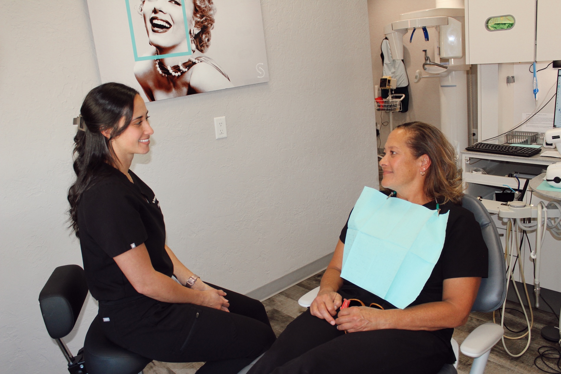 The image shows two people sitting in a dental office setting  one appears to be a patient with a mouthpiece on, and the other seems to be a dental professional engaged in conversation with the patient.