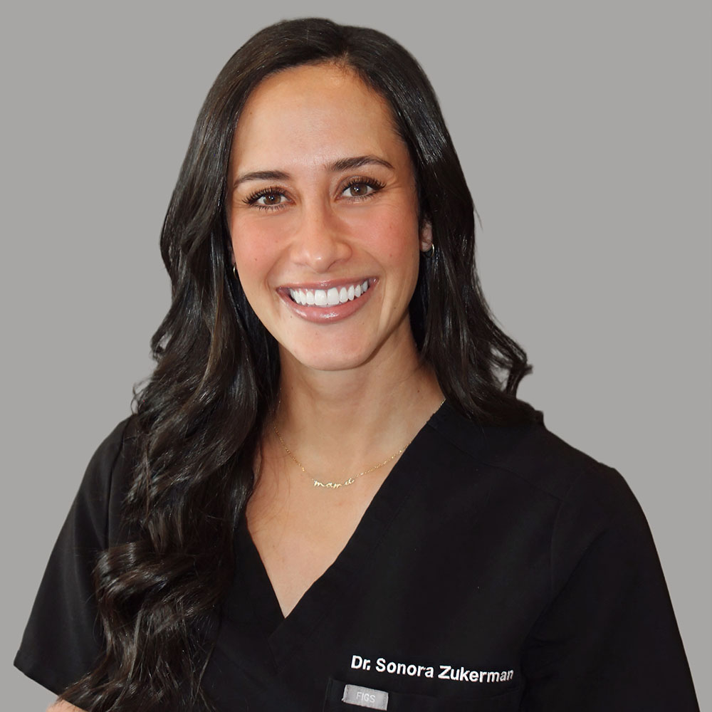The image shows a smiling woman with long hair wearing a stethoscope around her neck, standing against a light background.