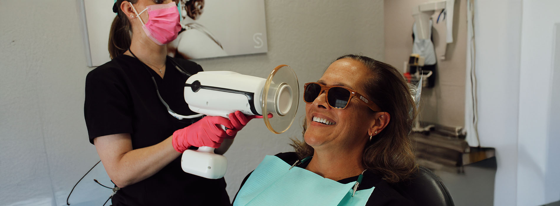 The image is a photograph of a woman with light skin, smiling at the camera. She appears to be in her late twenties or early thirties and has long hair. Her eyes are looking directly at the camera, and she is holding up her index finger near her mouth as if she s making a point or emphasizing something. The background is plain and light-colored, which suggests that this could be a stock photo used for various purposes such as advertising, personal branding, or lifestyle content.