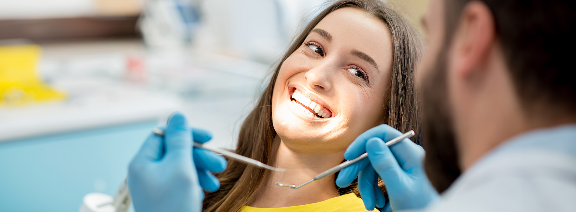 A person is seated in a dental chair, receiving care from a dental professional who stands behind them.