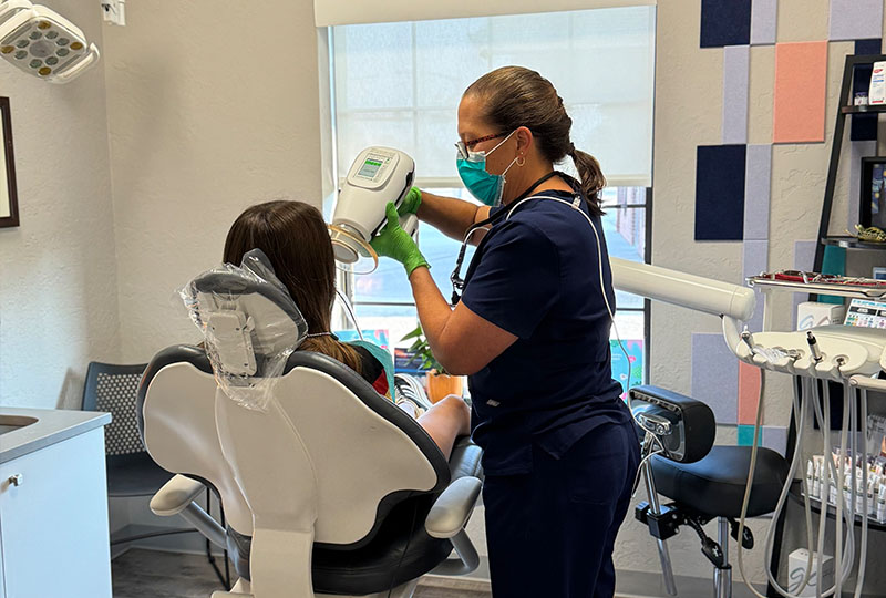 A dental hygienist in an office setting is cleaning a patient's teeth with a dental machine.