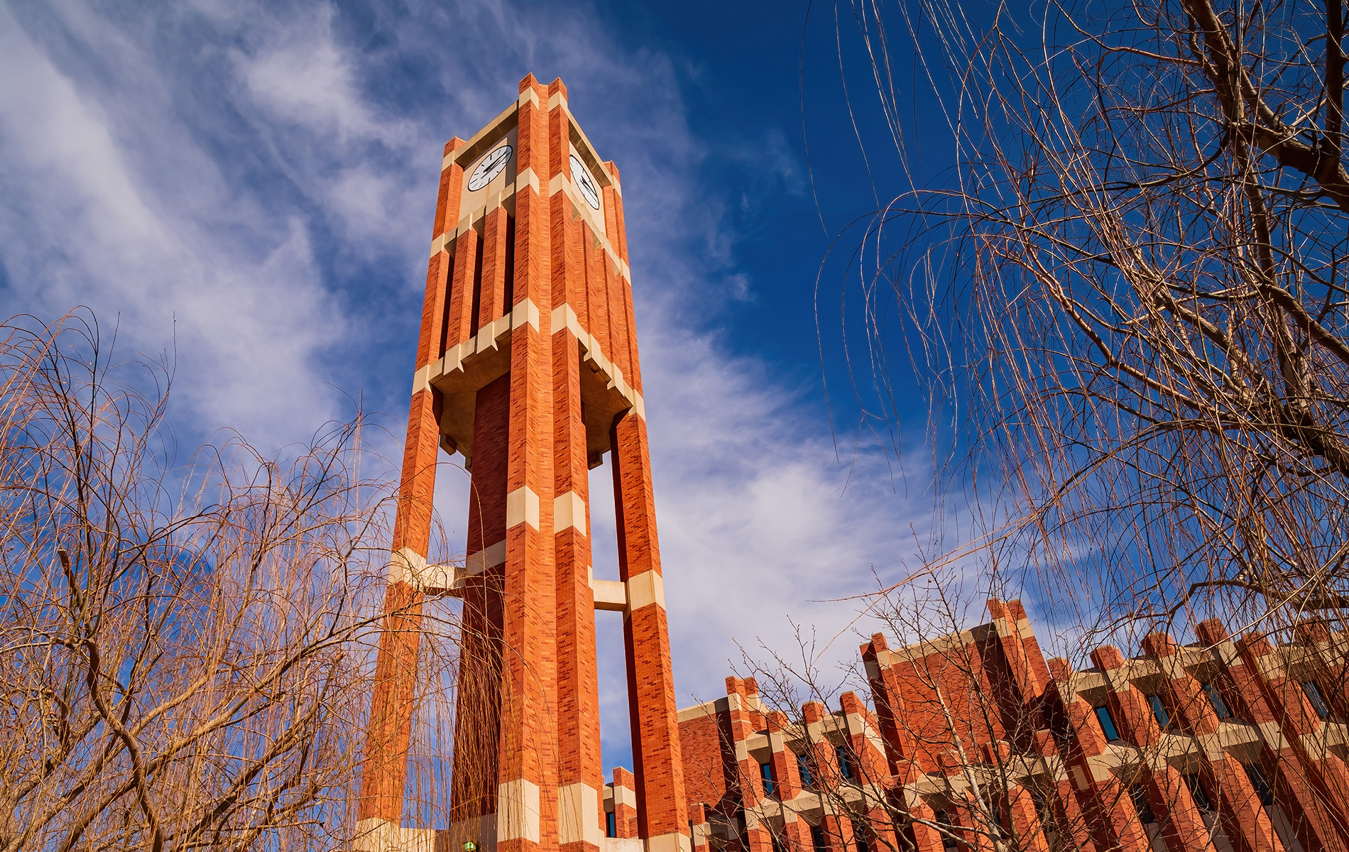 The image shows a tall brick clock tower with a white steeple, set against a clear blue sky with some scattered clouds.