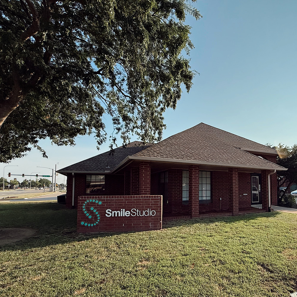 The image displays a brick building with a sign that reads  SMILE STUDIO  in front of a tree under a clear blue sky, showcasing the entrance to a business establishment.