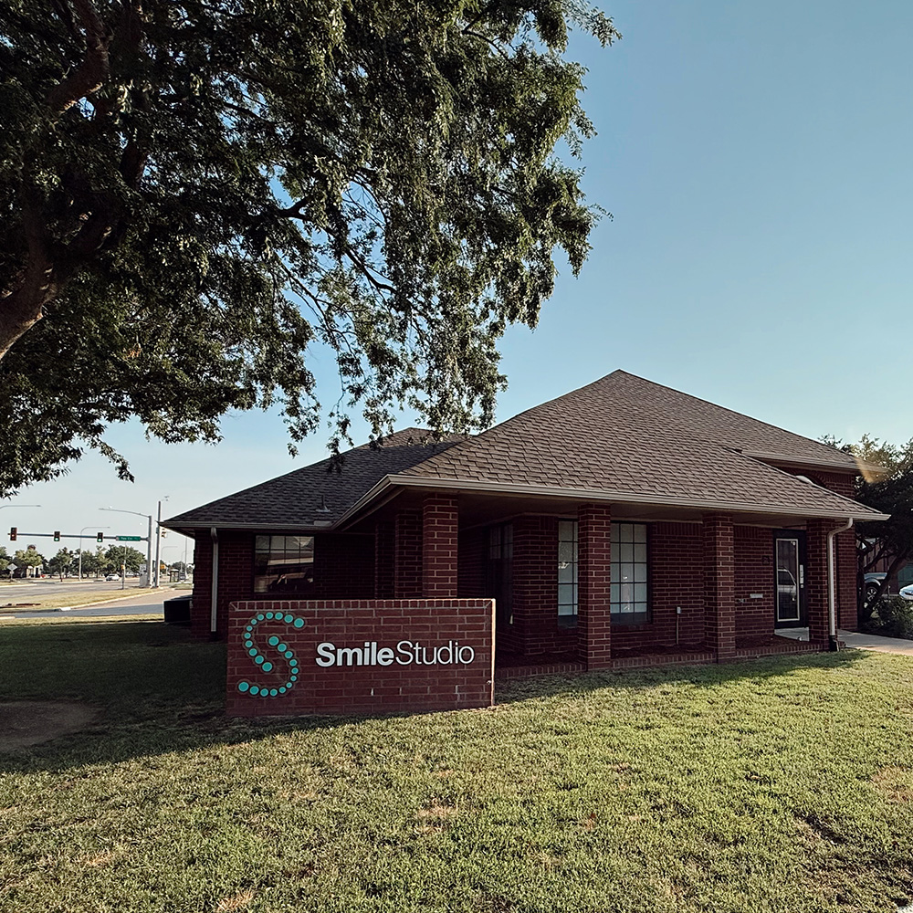 The image shows a building with a sign that reads  Smile Studio,  indicating it s a dental practice, set against a clear sky with some clouds and trees in the background.