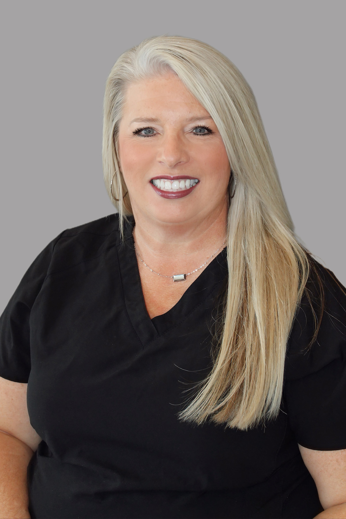 The image features a woman with blonde hair wearing a black shirt and a necklace, posing for a professional portrait with a neutral background.