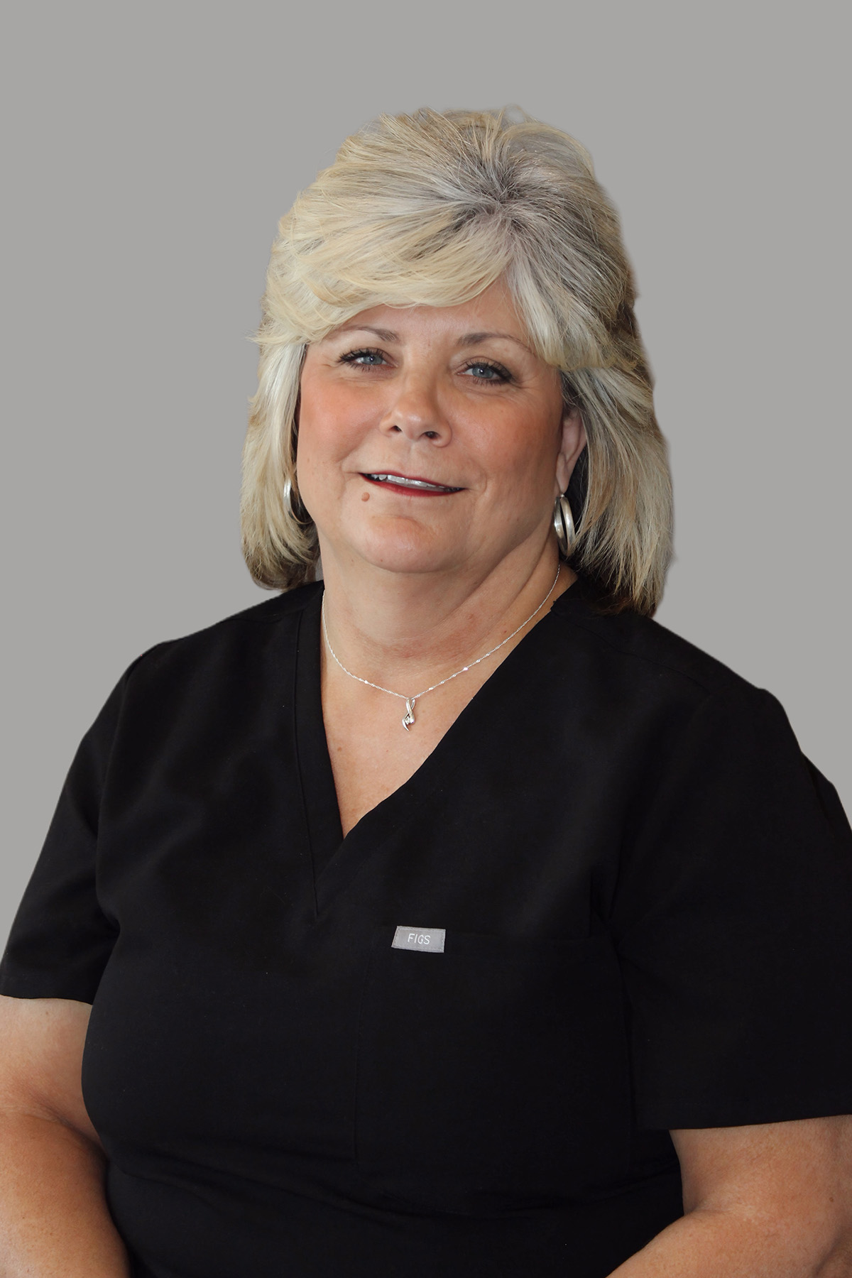 The image features a woman with blonde hair wearing glasses, a black top, and a name tag, posing for a portrait-style photo.