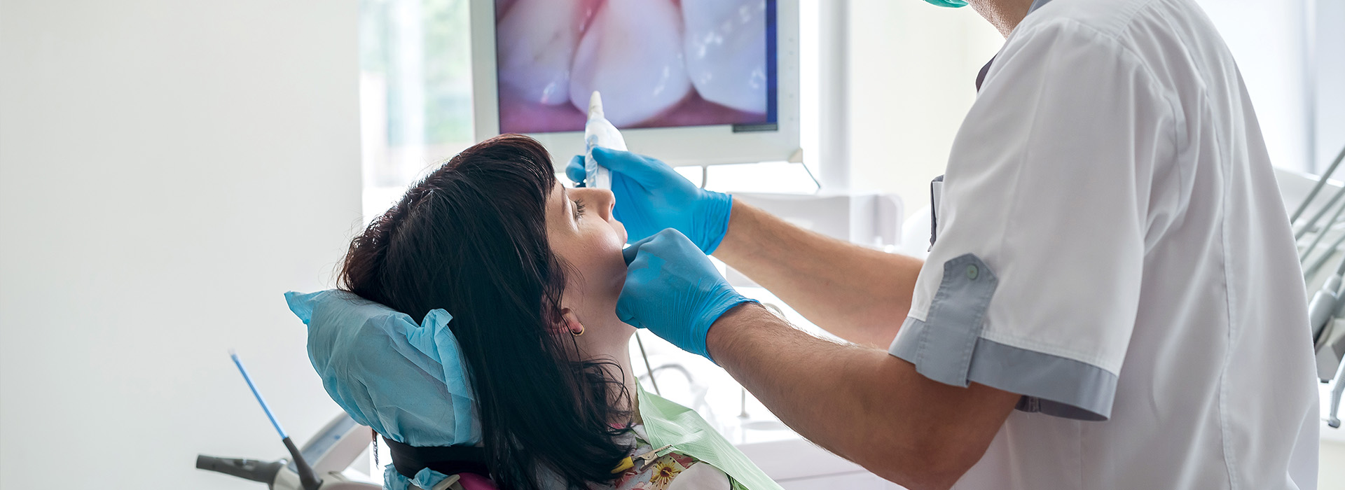 The image shows a dental professional performing a procedure on a patient s mouth with the use of dental instruments and tools, while the patient is seated in a dental chair.
