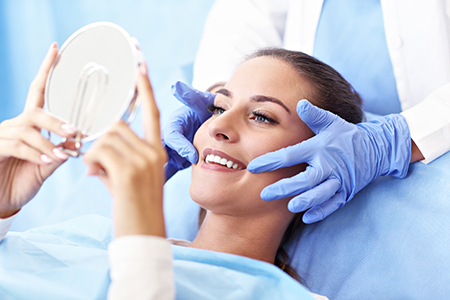 A woman receiving a facial treatment with a magnifying glass, while a professional attends to her with a smiling expression.